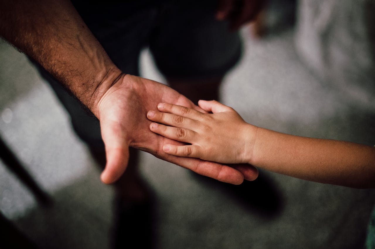 a child placing their hand in the palm of an adult standing next to them
