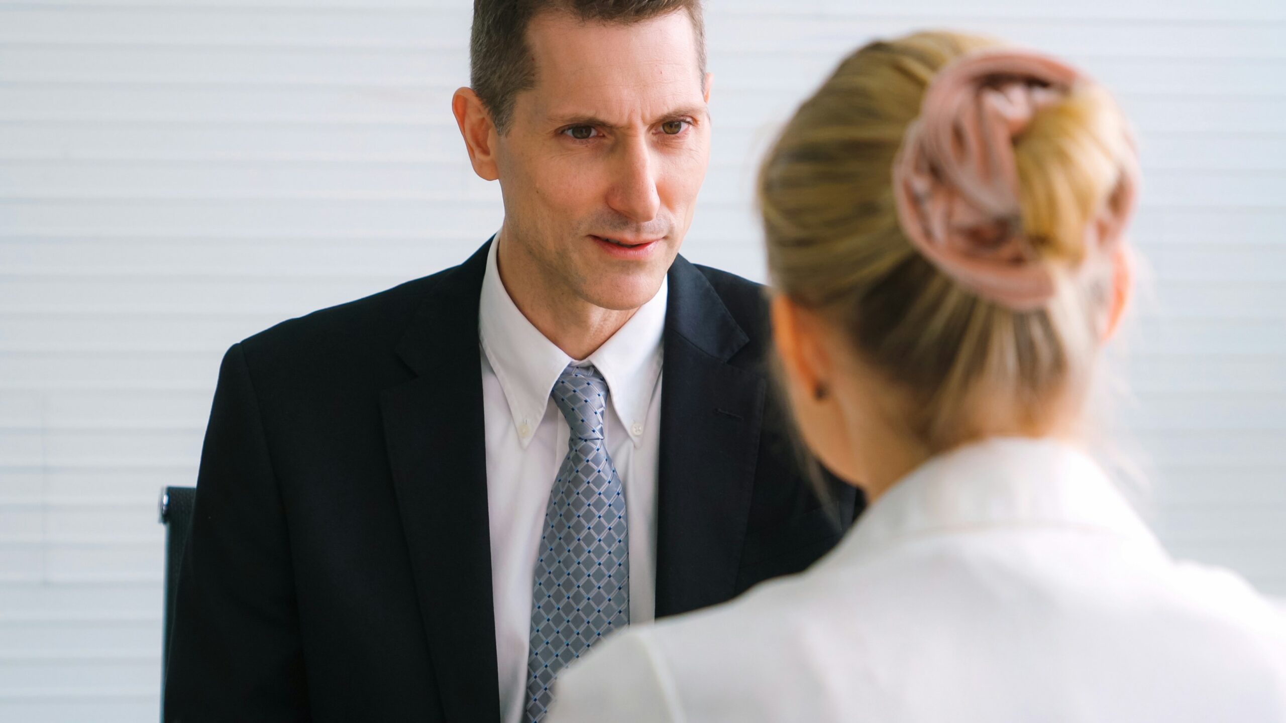 A man in a suit converses with a woman in a professional setting. - Pinkham & Associates, APLC A man in a suit converses with a woman in a professional setting.