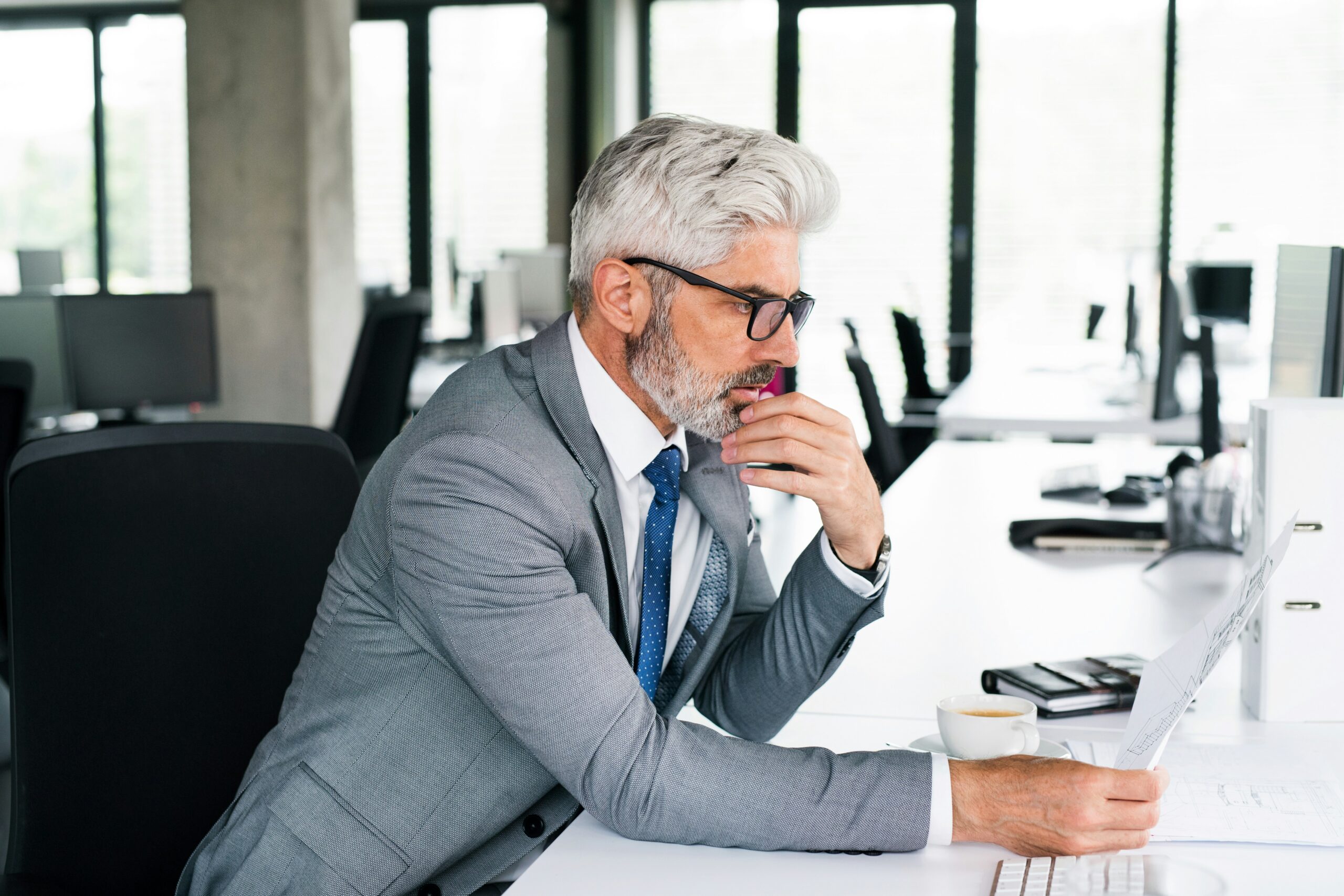 A man in a suit and glasses sits at a desk, working on a laptop. - Pinkham & Associates, APLC A man in a suit and glasses sits at a desk, working on a laptop.