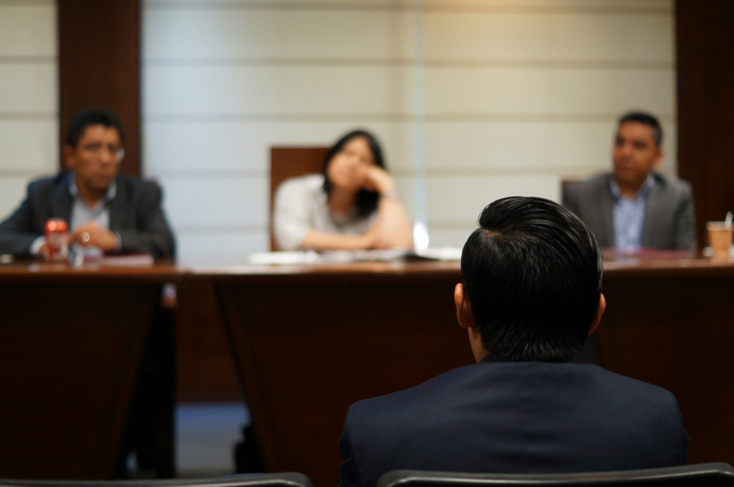 A man seated at a conference table in a meeting room, engaged in discussion with others. - Pinkham & Associates, APLC A man seated at a conference table in a meeting room, engaged in discussion with others.